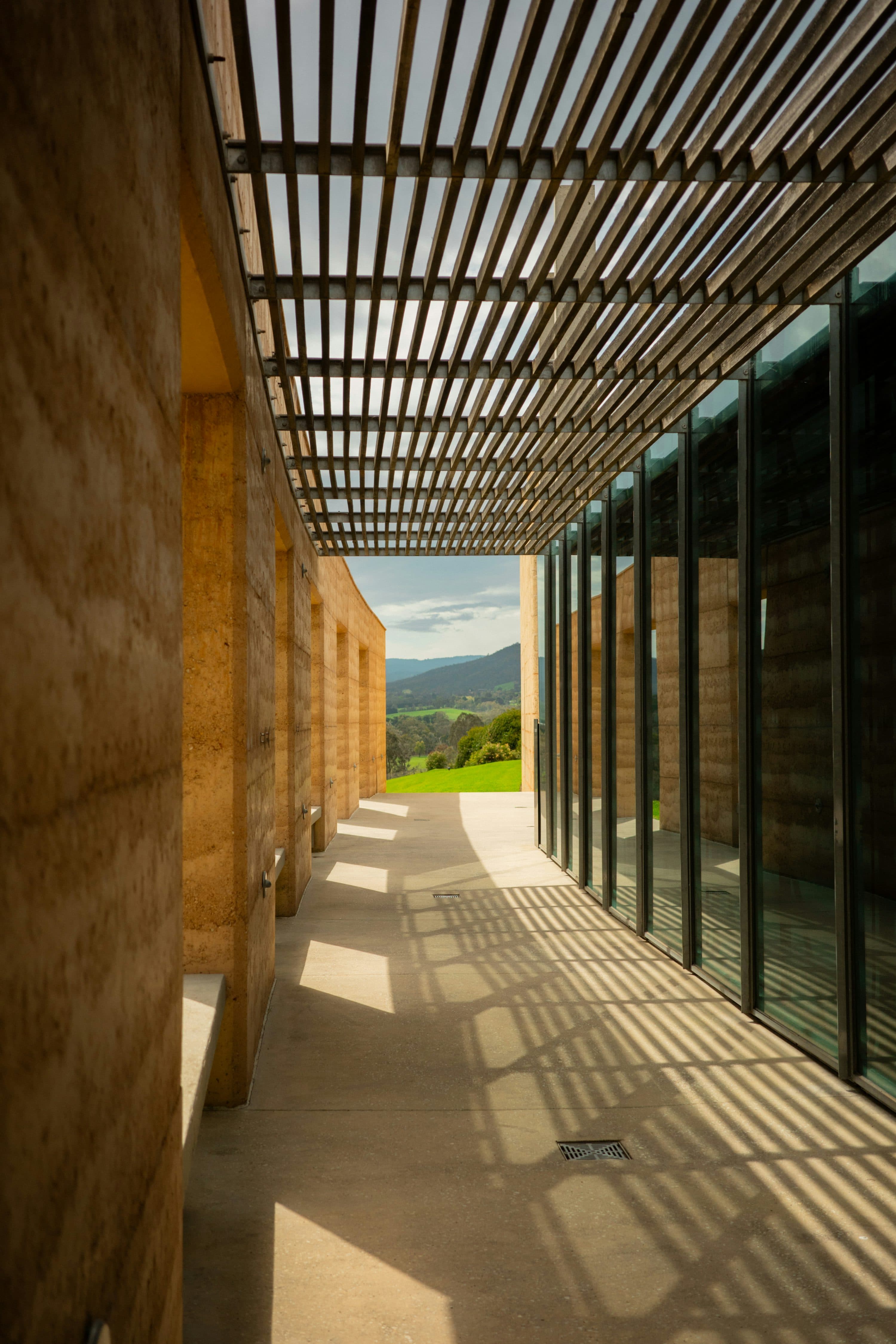 Contemporary rammed-earth walls beneath a timber pergola.