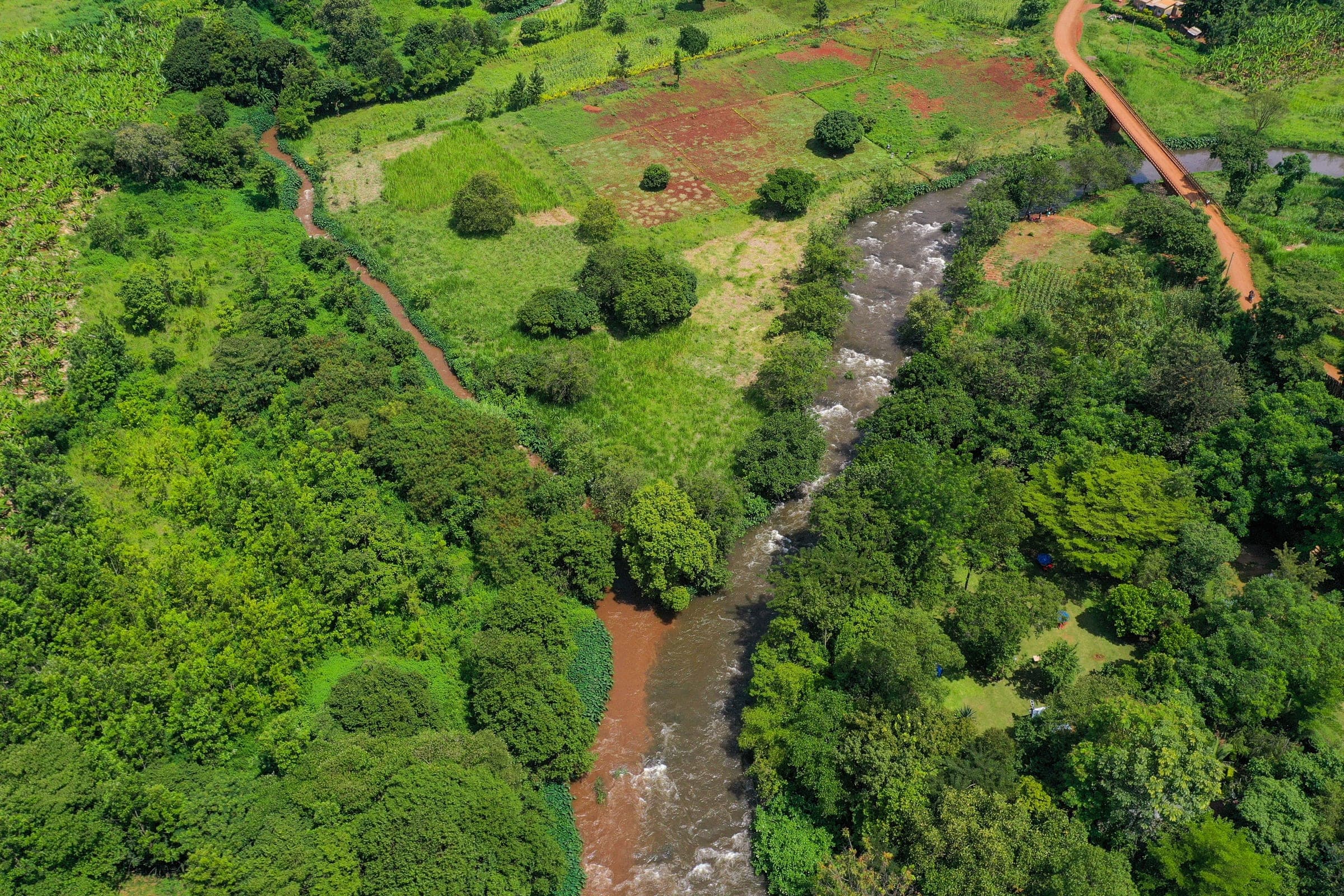 Aerial view of a river through farmland and red-earth tracks near Kutus, Kirinyaga County, Kenya.